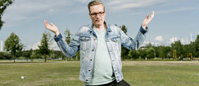 Professori Tuukka Saarimaa seisomassa tyhjällä nurmikentällä, joka sijaitsee Helsingin keskustassa Oodi-kirjaston ja musiikkitalon välisellä puistoalueella. Kuvaaja: Jaakko Kahilaniemi.