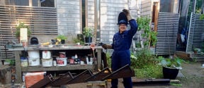 Woman welding in blue overalls and protective gear in a yard