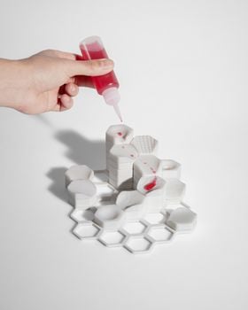 A hand squeezing a red liquid on top of the white hexagonal sculpture