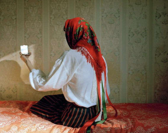 A woman in slavic clothing looking in the mirror with her back turnes